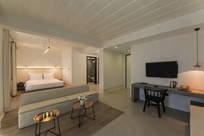 Una habitación de hotel moderna con cama, sofá, zona de comedor y televisor.