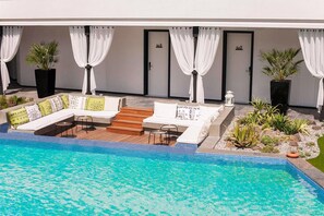 Zona junto a la piscina con mobiliario, una terraza de madera y una piscina.