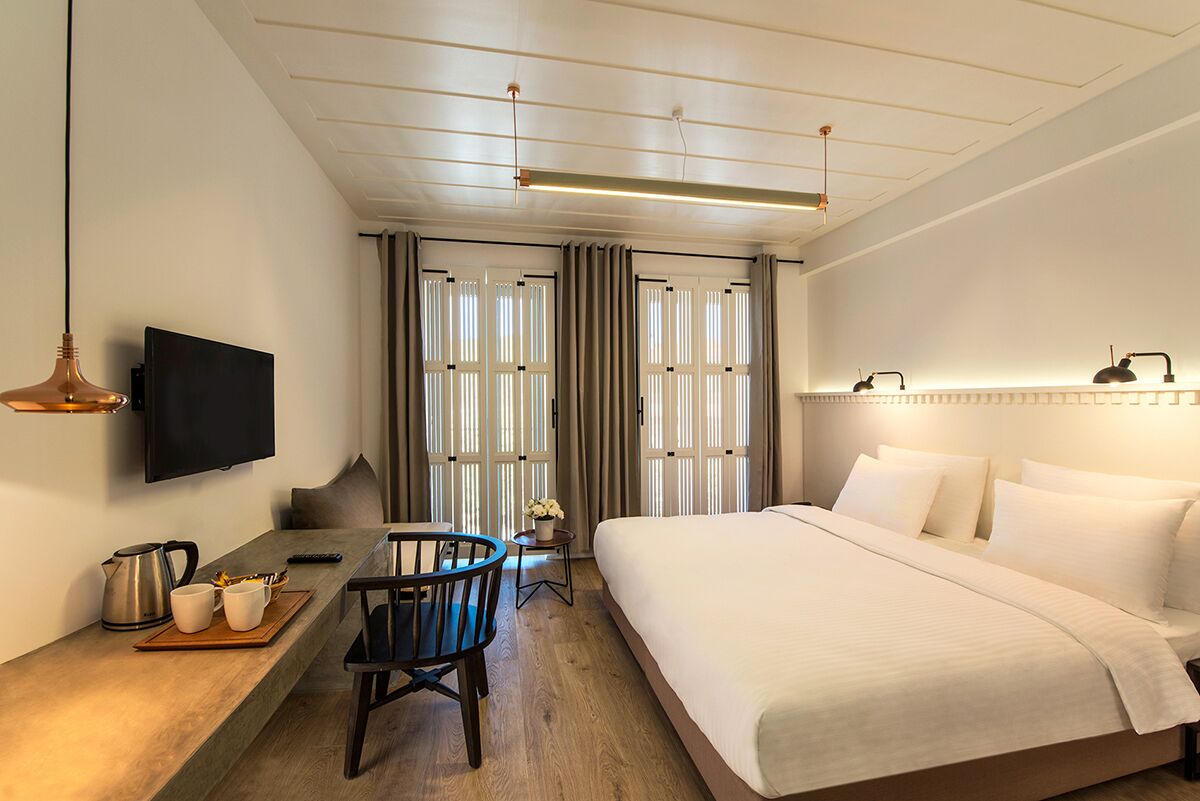 A hotel room with a bed, a desk with a chair, a television, and a window with curtains.