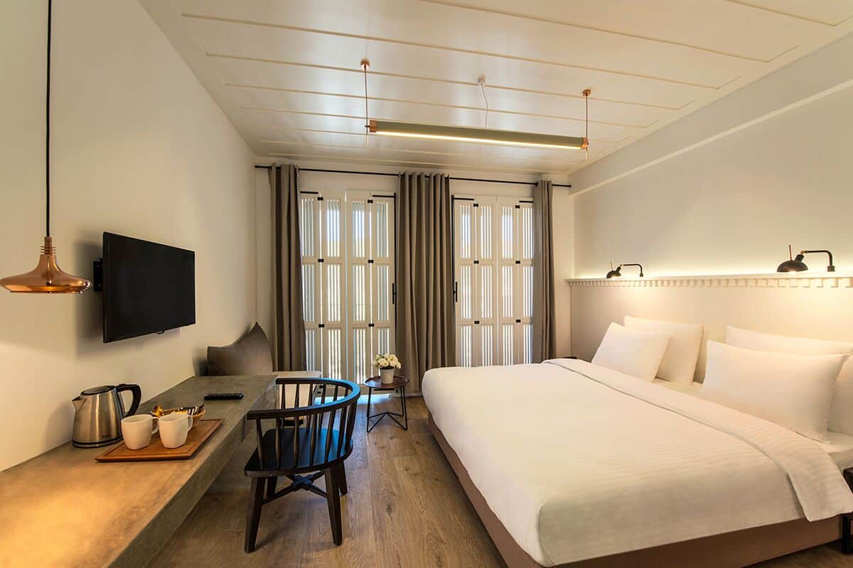 A hotel room with a bed, a desk with a chair, a television, and a window with curtains.
