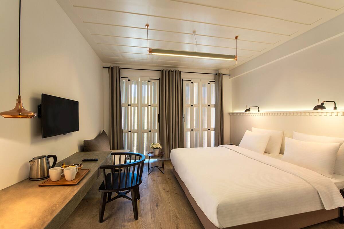 Habitación de hotel con cama, escritorio con silla, televisión y ventana con cortinas.