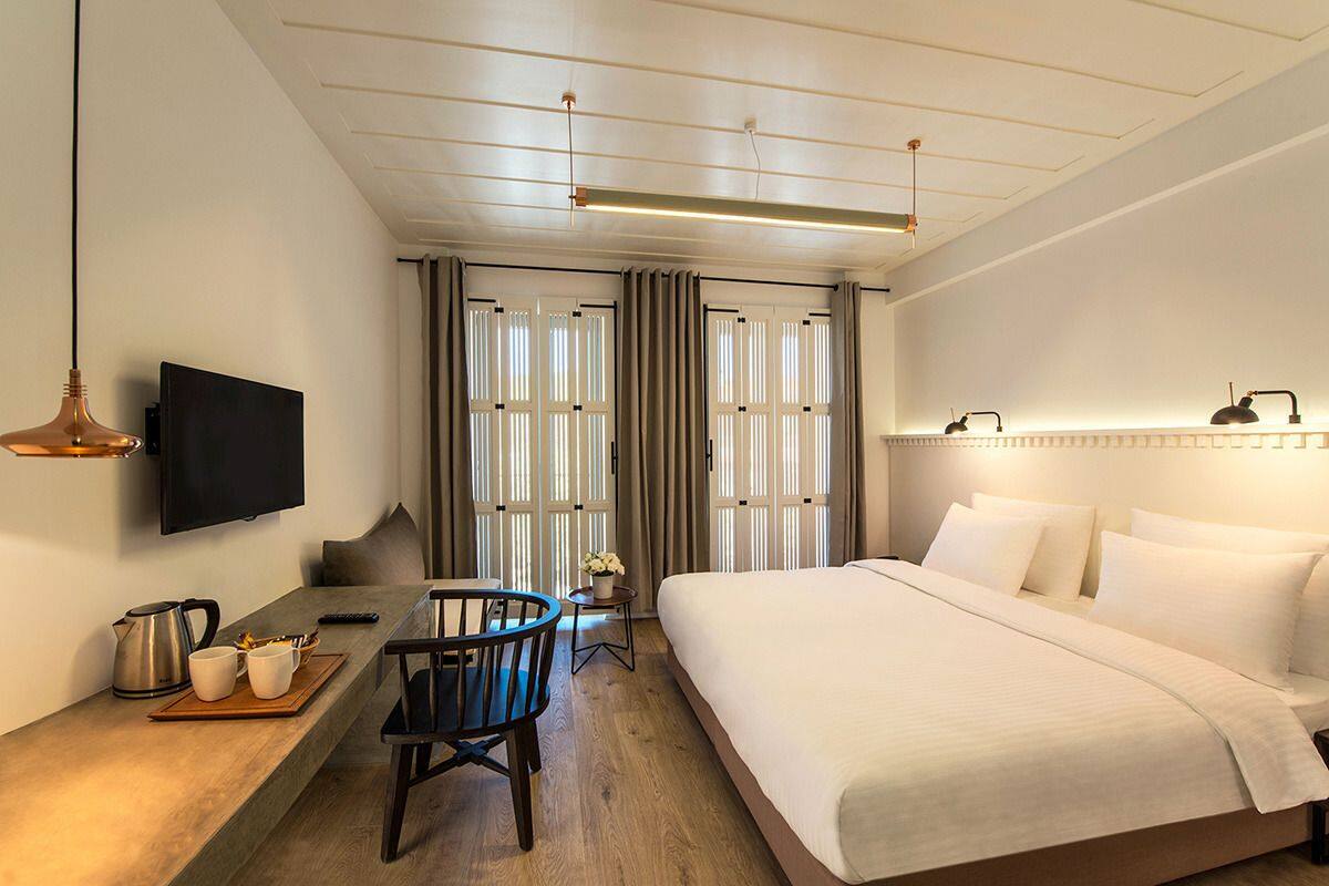 Una habitación de hotel con una cama, un escritorio con silla, televisor y ventana con cortinas.
