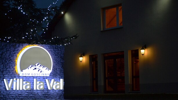 Un edificio con pared de piedra y un letrero circular con un logotipo de montaña y el texto "Villa la Val Dom Goscinny".