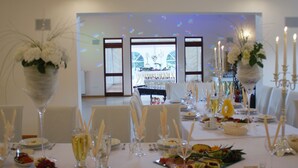 Un comedor formal con mesas dispuestas para una comida, con manteles blancos, cristalería y centros de mesa florales.