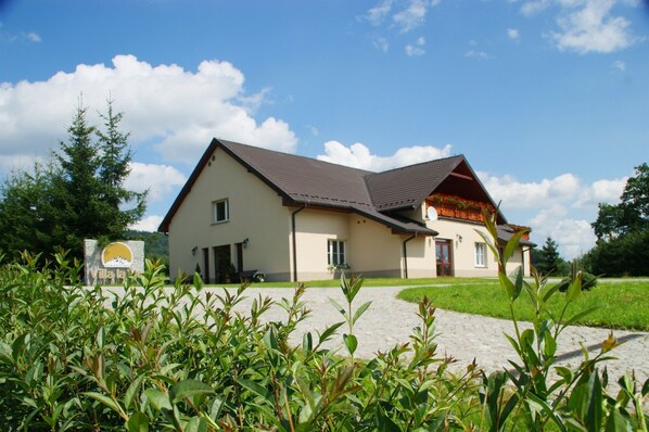 A two-story house with a sloped roof, a visible porch, and a paved driveway. - Villa la Val (Kamienna Gora)