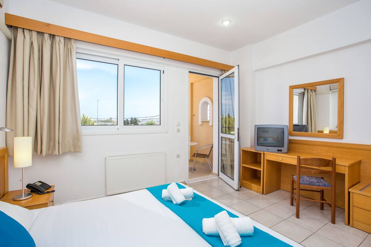 Habitación de hotel con cama, escritorio, silla, televisión y baño visible a través de una puerta abierta.