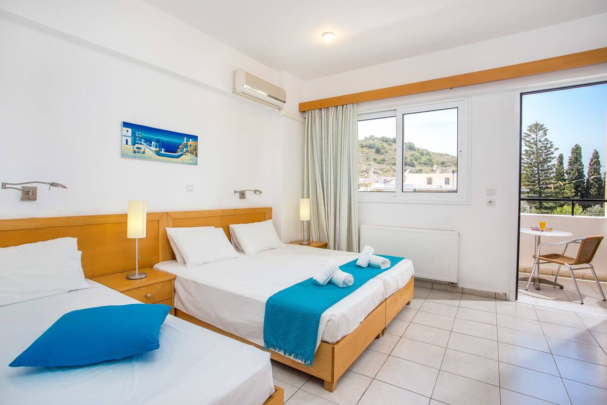 Habitación de hotel con dos camas, un balcón y vistas al paisaje.