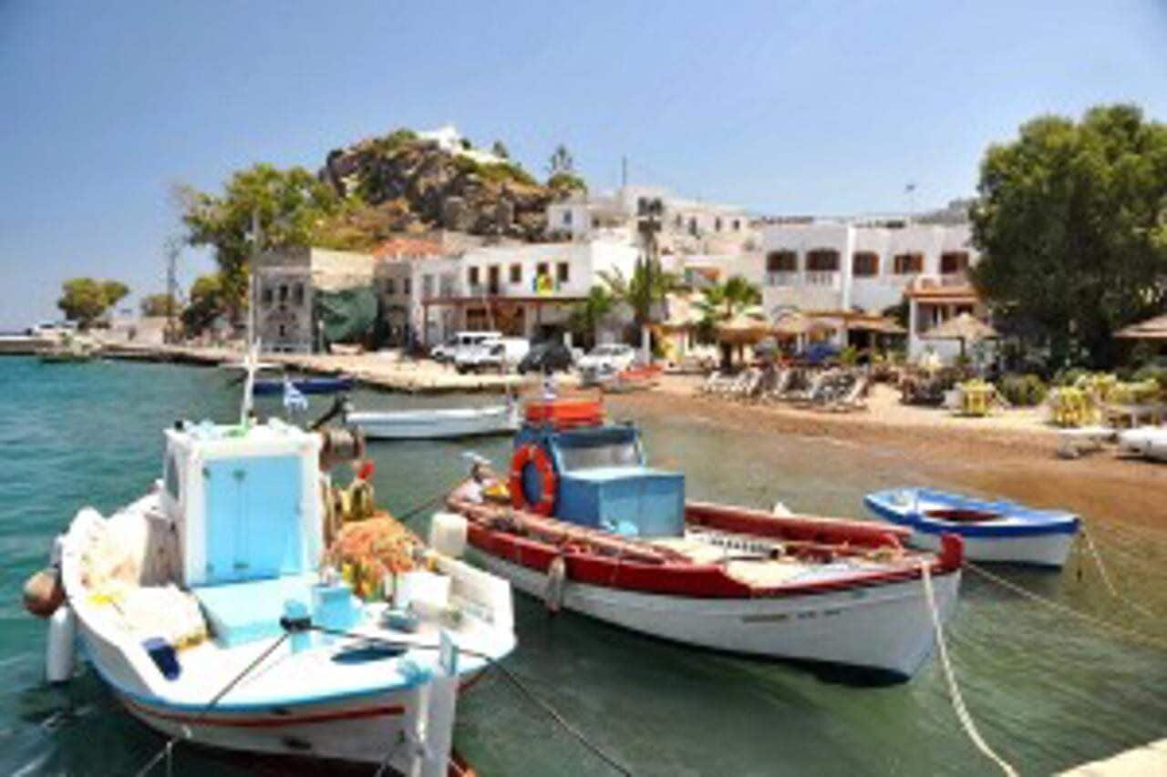 A coastal town with boats docked at the harbor, buildings with balconies, and a clear sky.