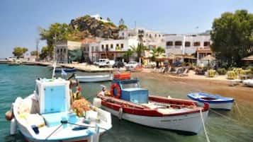 A coastal town with boats docked at the harbor, buildings with balconies, and a clear sky.