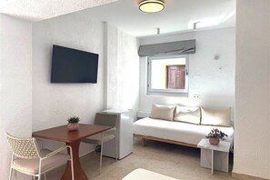 A compact room with a bed, a small table, a chair, a TV mounted on the wall, and a window with a view.