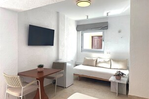 Habitación pequeña con cama, una mesita, una silla, televisor montado en la pared y ventana con vistas.