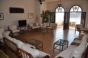 A spacious living room with a large sofa, armchairs, a television, and a view of the sea through arched windows.