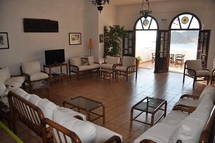 Amplia sala de estar con un sofá grande, sillones, televisor y vista al mar a través de ventanales de arco.