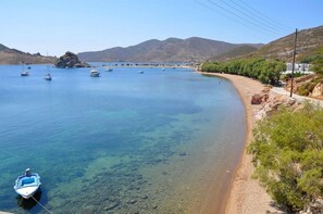 A coastal scene with boats on calm water, a sandy beach, and a mountainous backdrop.