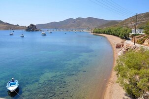 A coastal scene with boats on calm water, a sandy beach, and a mountainous backdrop.