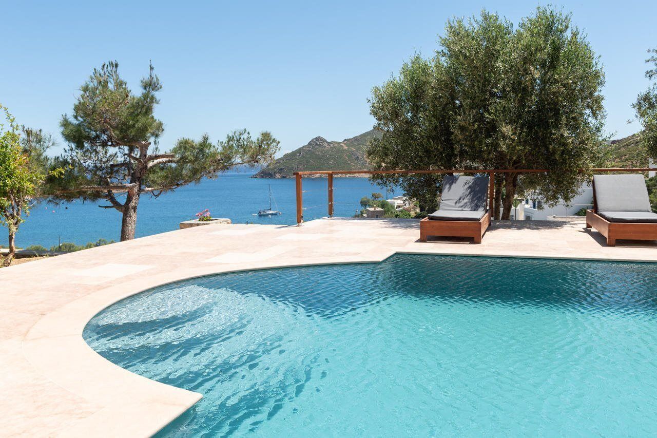 A swimming pool with lounge chairs and a pergola, overlooking a body of water and hills.
