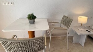 Un petit coin repas comprenant une table, deux chaises, une plante en pot, une lampe et une prise électrique.
