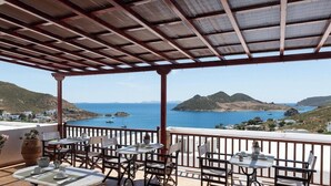 Une terrasse agrémentée de tables et de chaises, offrant une vue sur un paysage côtier avec des collines et la mer.