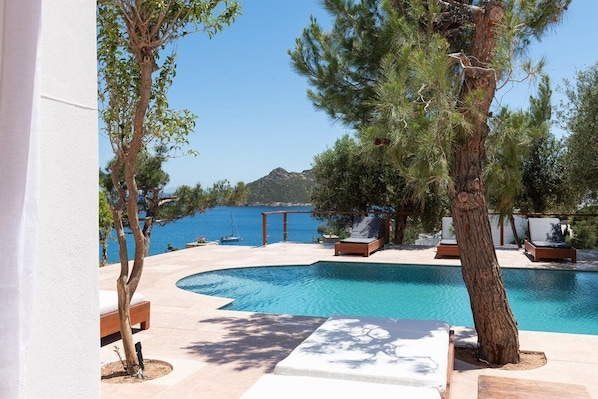 A pool area with lounge chairs and a view of the sea.