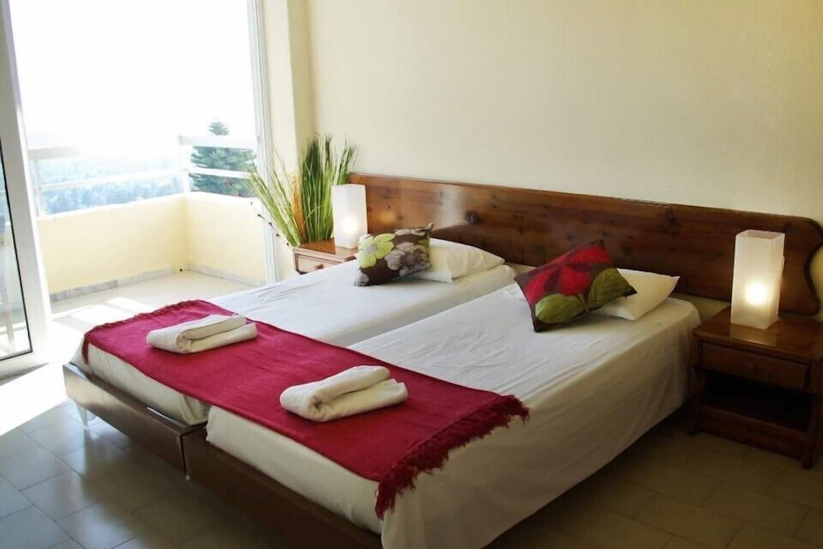 Un lit double avec une tête de lit en bois, deux tables de chevet, une lampe de chevet et un balcon avec vue.
