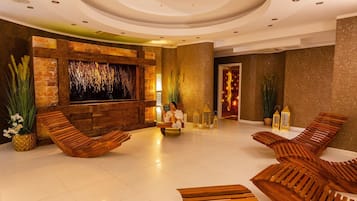 A modern lobby with wooden lounge chairs, a stone wall with a textured wall art, and a large illuminated wall feature.