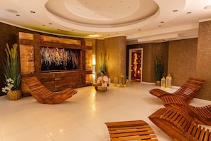 A modern lobby with wooden lounge chairs, a stone wall with a textured wall art, and a large illuminated wall feature.