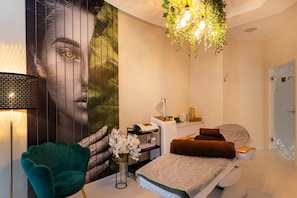 Un dormitorio moderno con un mural grande en la pared, una silla verde, una cama con toallas, una mesita de noche y una lámpara colgante.