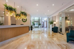 Un moderno vestíbulo de hotel con mostrador de recepción, un gran adorno verde y un ascensor de vidrio.