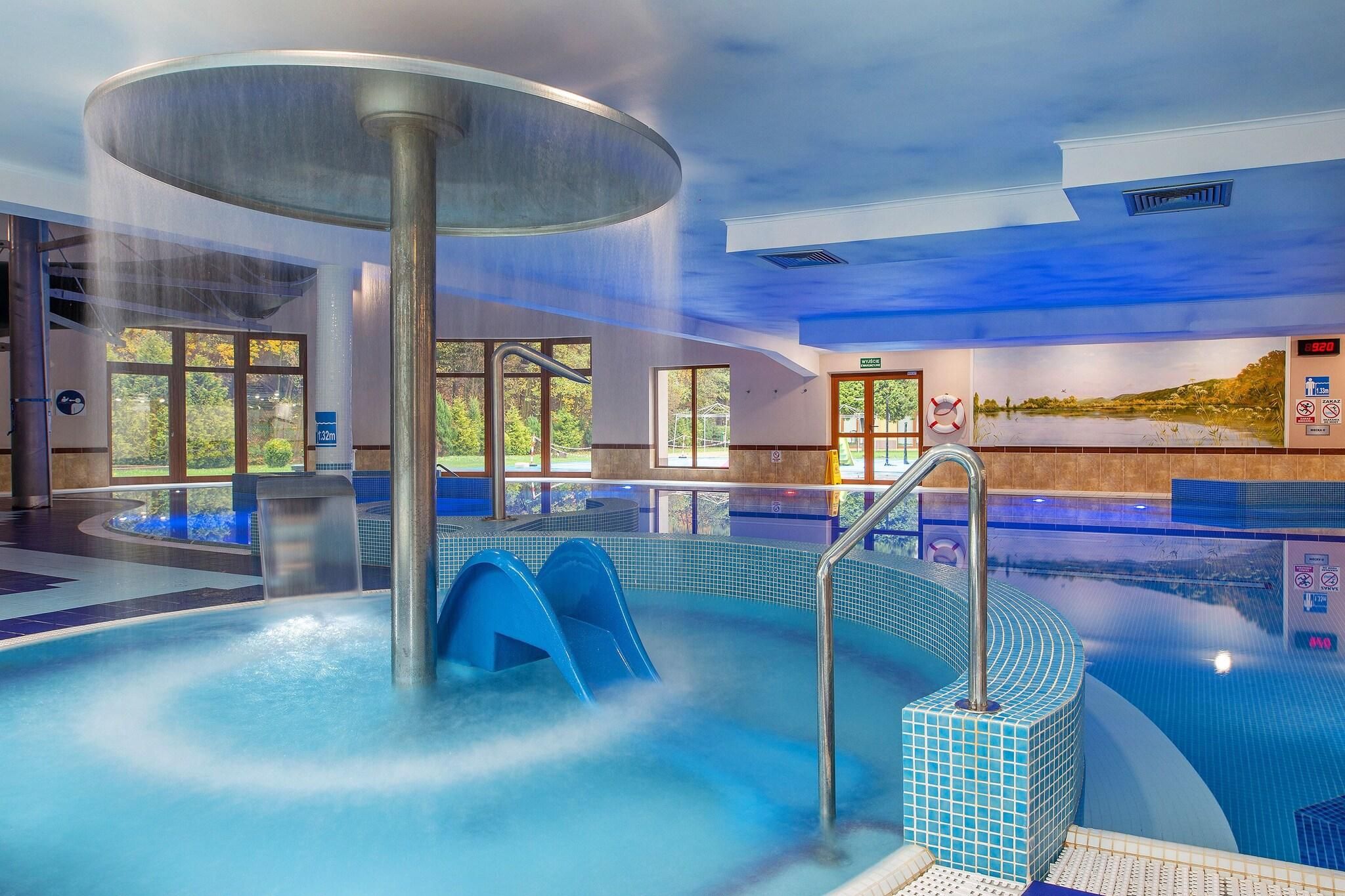 A large indoor swimming pool with a hot tub, clear glass walls, and a view of the outdoors.