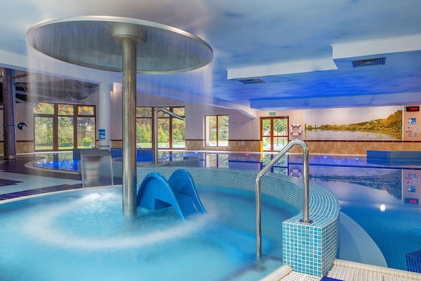 Una amplia piscina interior con jacuzzi, paredes de vidrio transparente y vistas al exterior.
