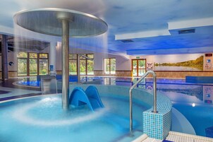 Una amplia piscina interior con jacuzzi, paredes de vidrio transparente y vistas al exterior.