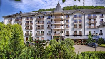 A multi-story hotel with balconies, a parking area, and a mountainous backdrop.
