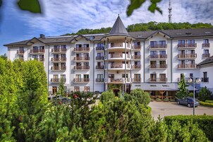 Un hotel de varios pisos con balcones, un estacionamiento y montañas al fondo.