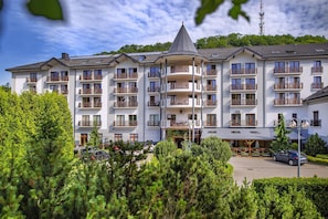 A multi-story hotel with balconies, a parking area, and a mountainous backdrop.