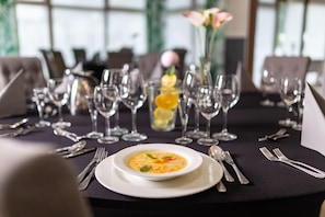 Una mesa de comedor dispuesta con un tazón blanco de sopa, cubiertos y copas de vino.
