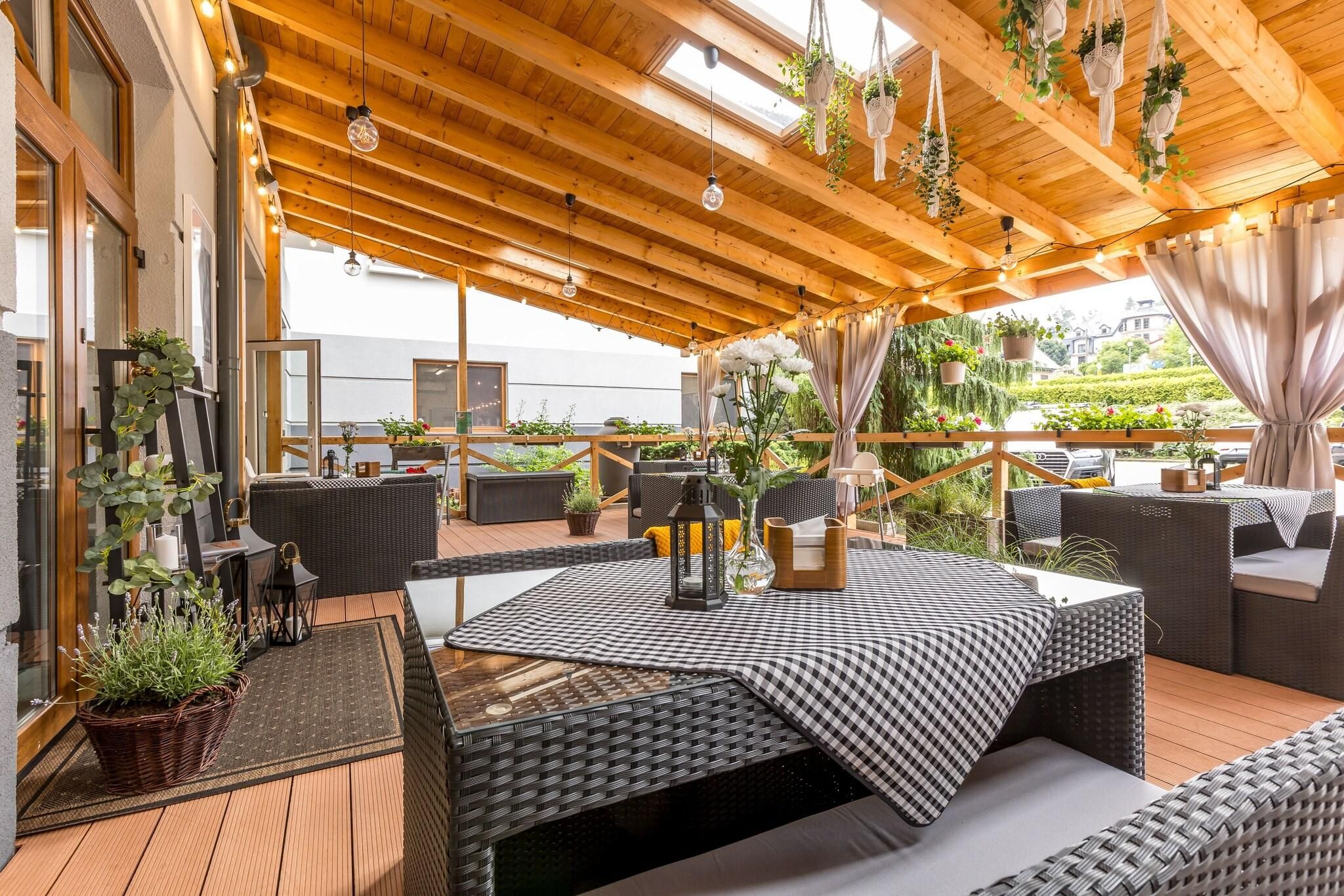 An outdoor patio with wooden flooring, wicker furniture, and hanging plants.