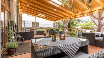 An outdoor patio with wooden flooring, wicker furniture, and hanging plants.