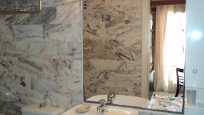 Une salle de bain avec un mur en marbre, un lavabo, un miroir et des toilettes.