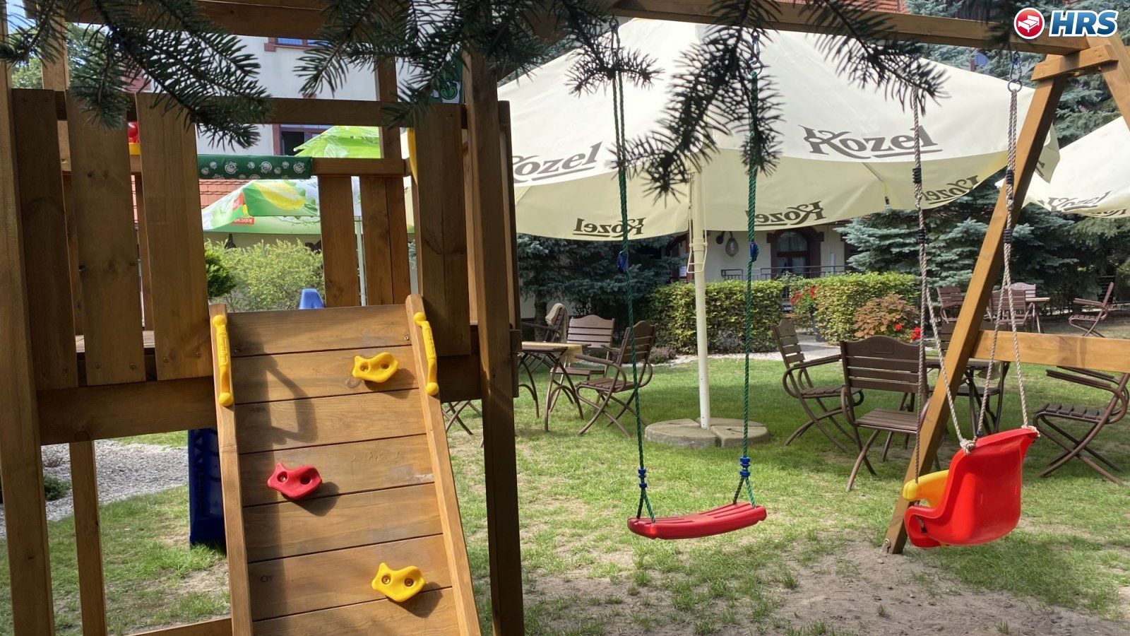 Un parque infantil con un muro de escalar de madera, columpios y un tobogán.