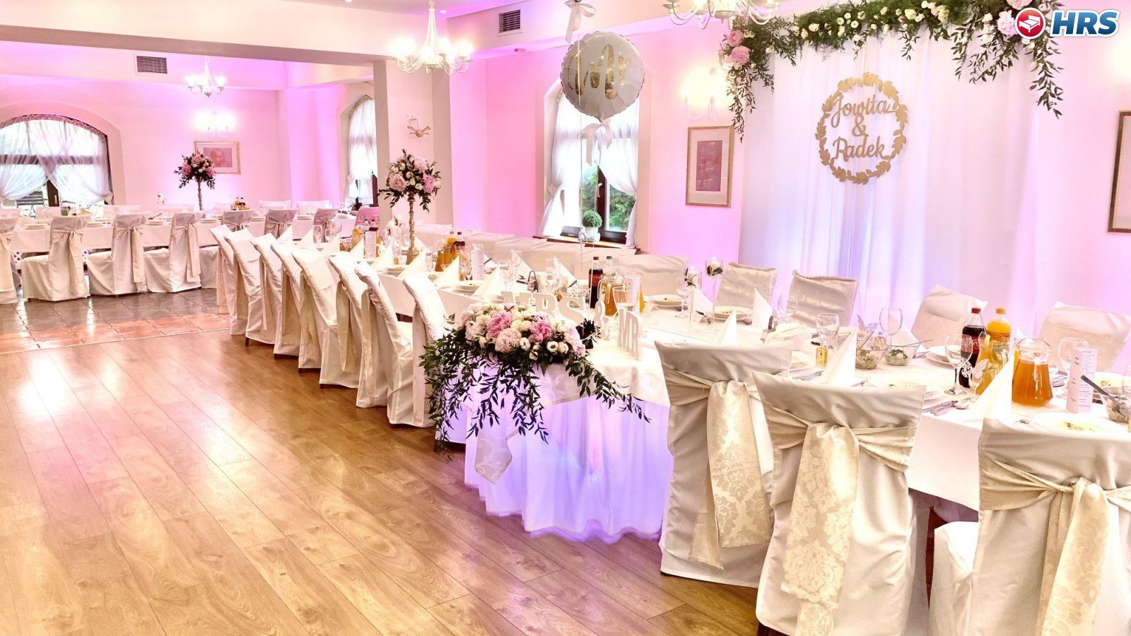 Un salón de banquetes con filas de mesas, cada una cubierta con mantel blanco y decorada con centros de mesa florales.