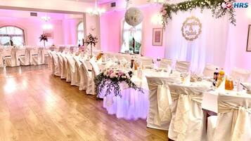 Un salón de banquetes con filas de mesas, cada una cubierta con mantel blanco y decorada con centros de mesa florales.