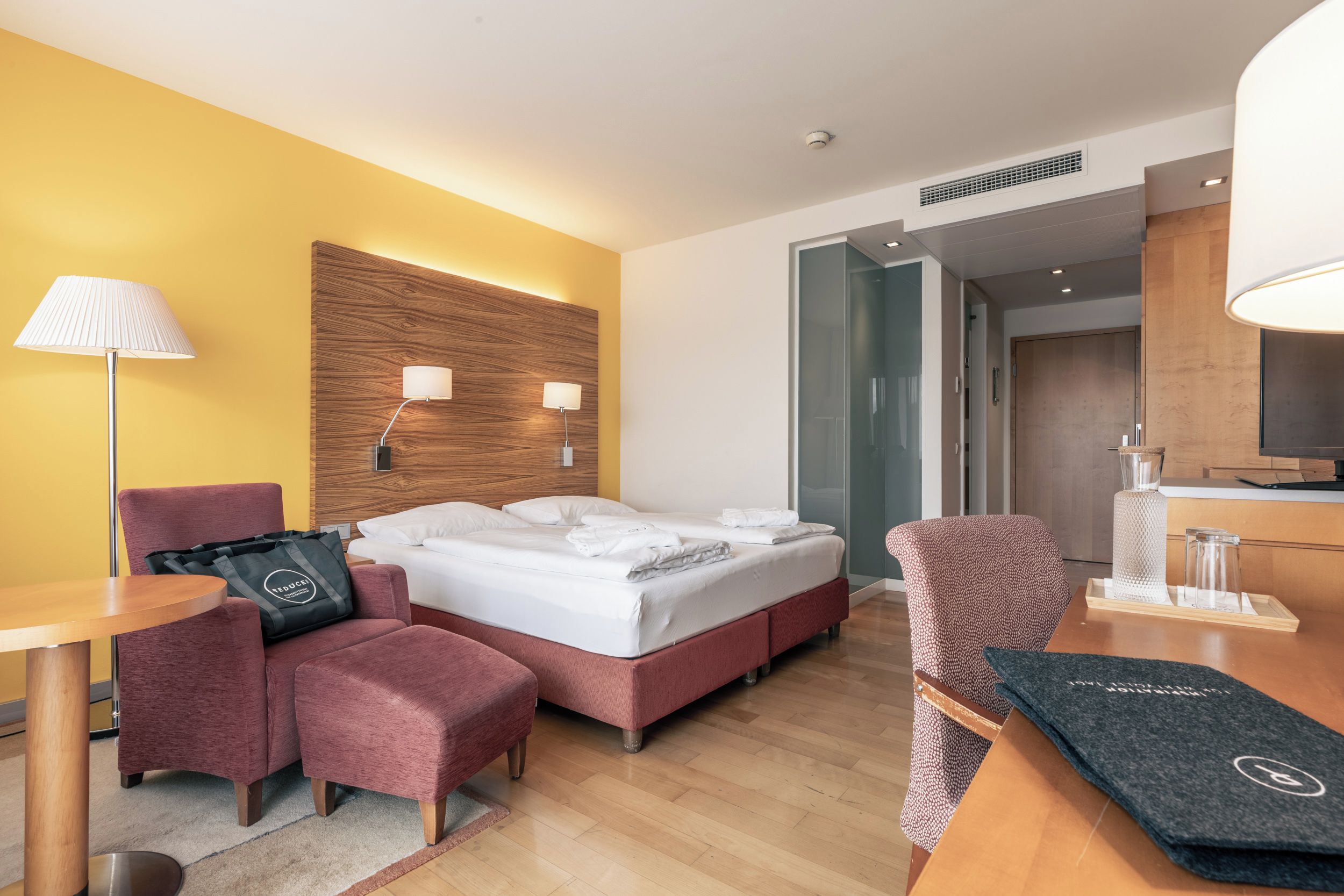 Habitación de hotel con cama, dos lámparas de noche, escritorio, silla, mesita y armario.