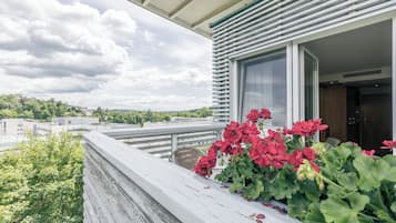 Un balcón con vistas a la ciudad, una ventana con vistas al cielo y una planta en maceta con flores rojas.
