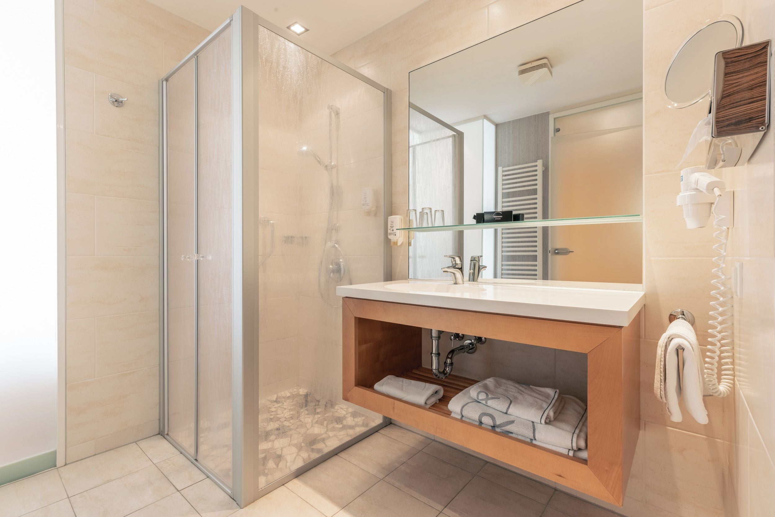 A modern bathroom with a glass-enclosed shower, a vanity with a mirror, and a towel rack.