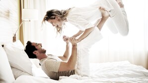A couple in a bedroom with a bed, pillows, and a bedside lamp. - Reduce Hotel Vital (Bad Tatzmannsdorf)