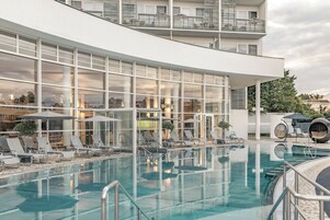 Un hotel moderno con una amplia piscina exterior, tumbonas y fachada de cristal.
