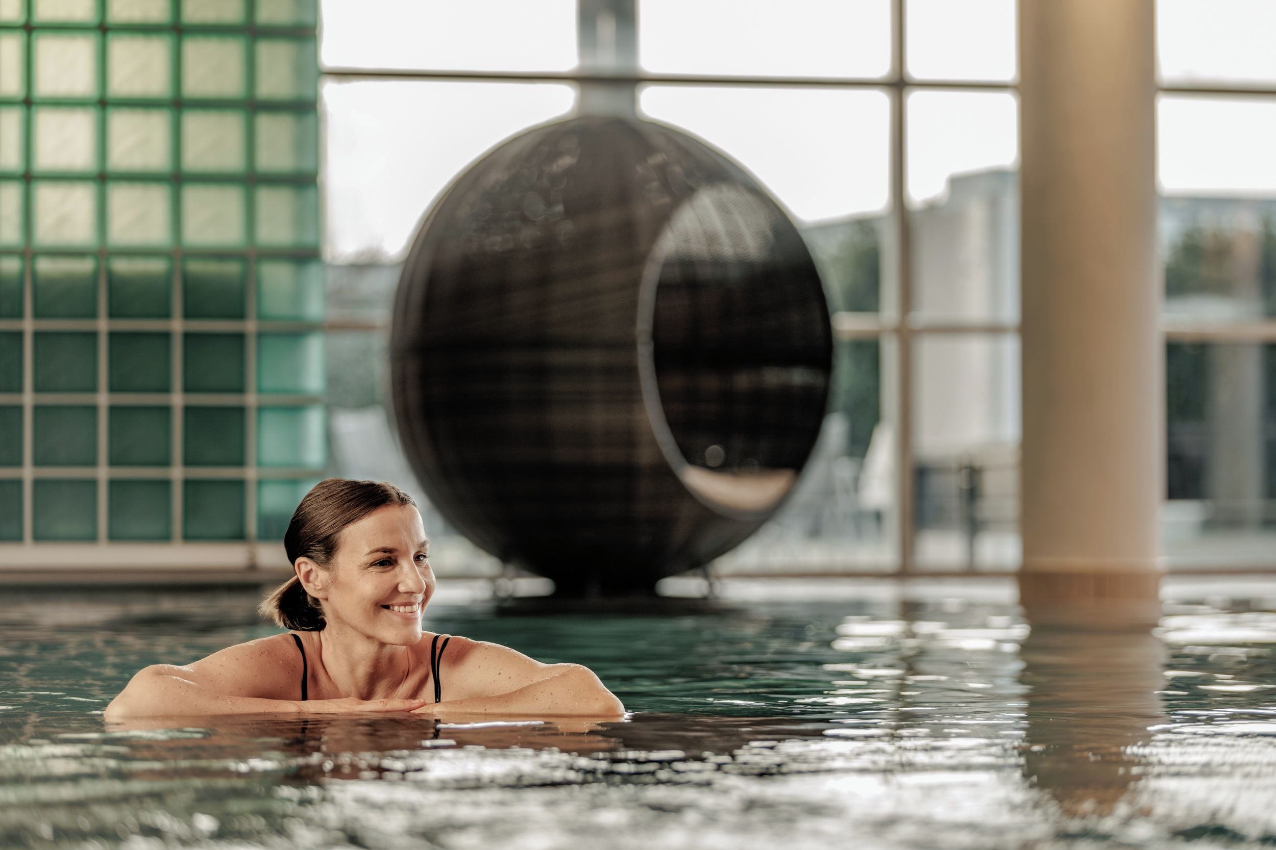 A person in a swimming pool with a large, circular, dark-colored structure in the background.