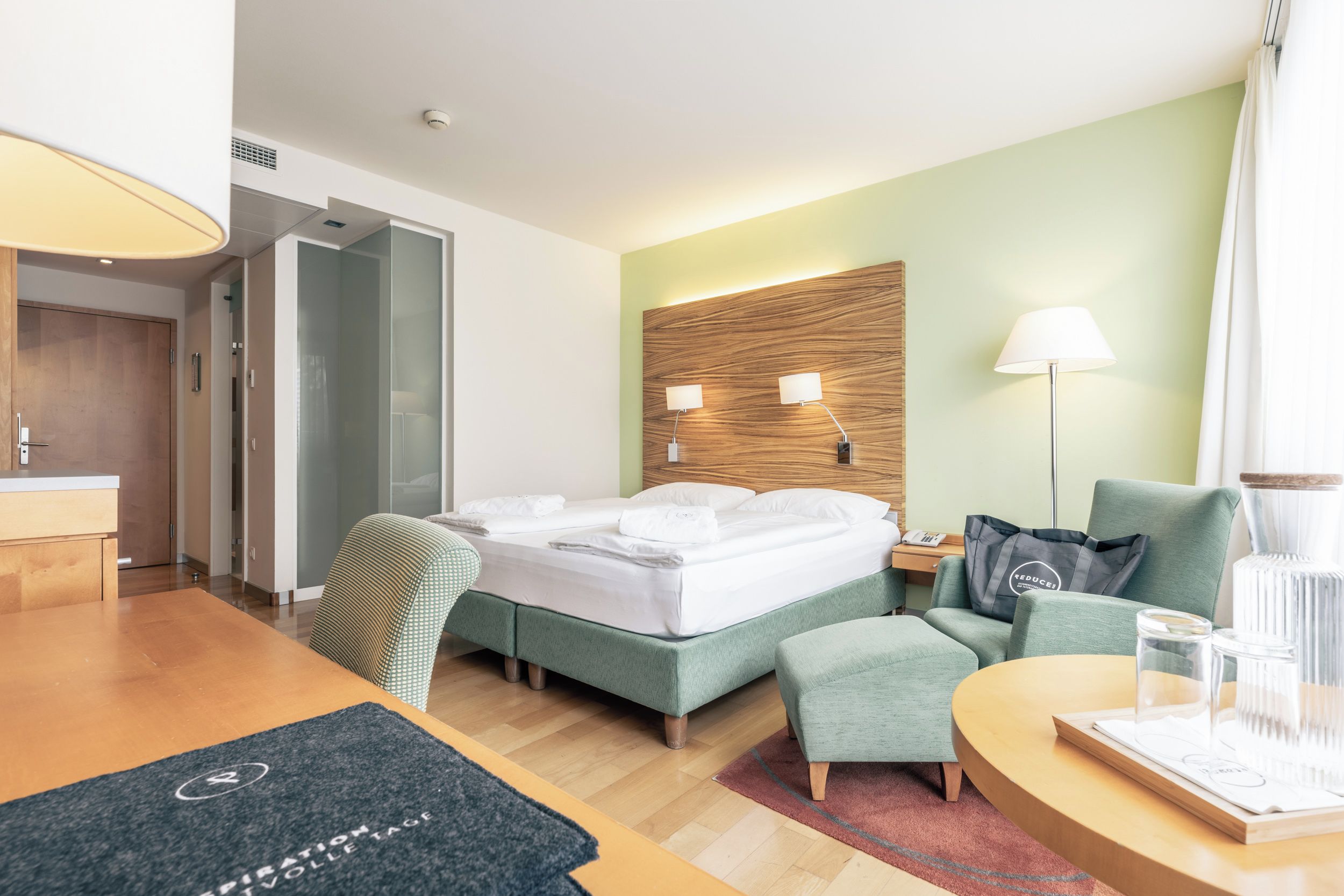 Habitación de hotel con cama, escritorio, silla, sofá, lámpara y mesita de noche.