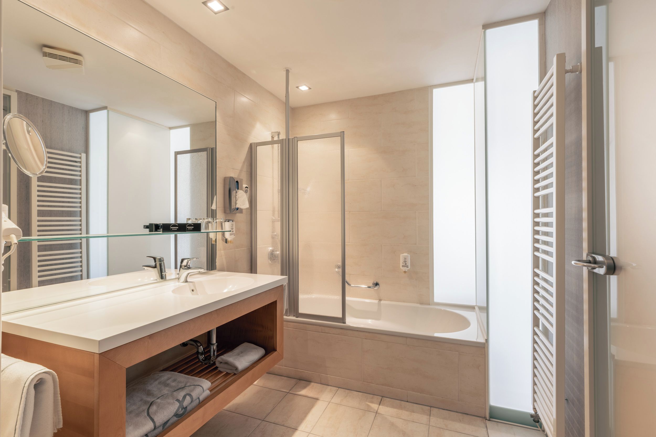 Un baño moderno con un espejo grande, lavamanos dobles, cabina de ducha de vidrio y una bañera.