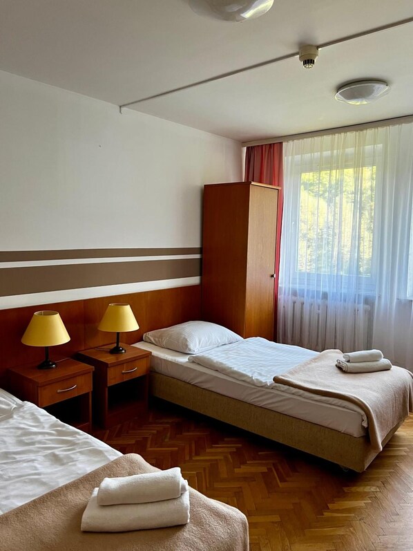Ett hotellrum med två sängar, en garderob, ett skrivbord med lampor och ett fönster med gardiner.